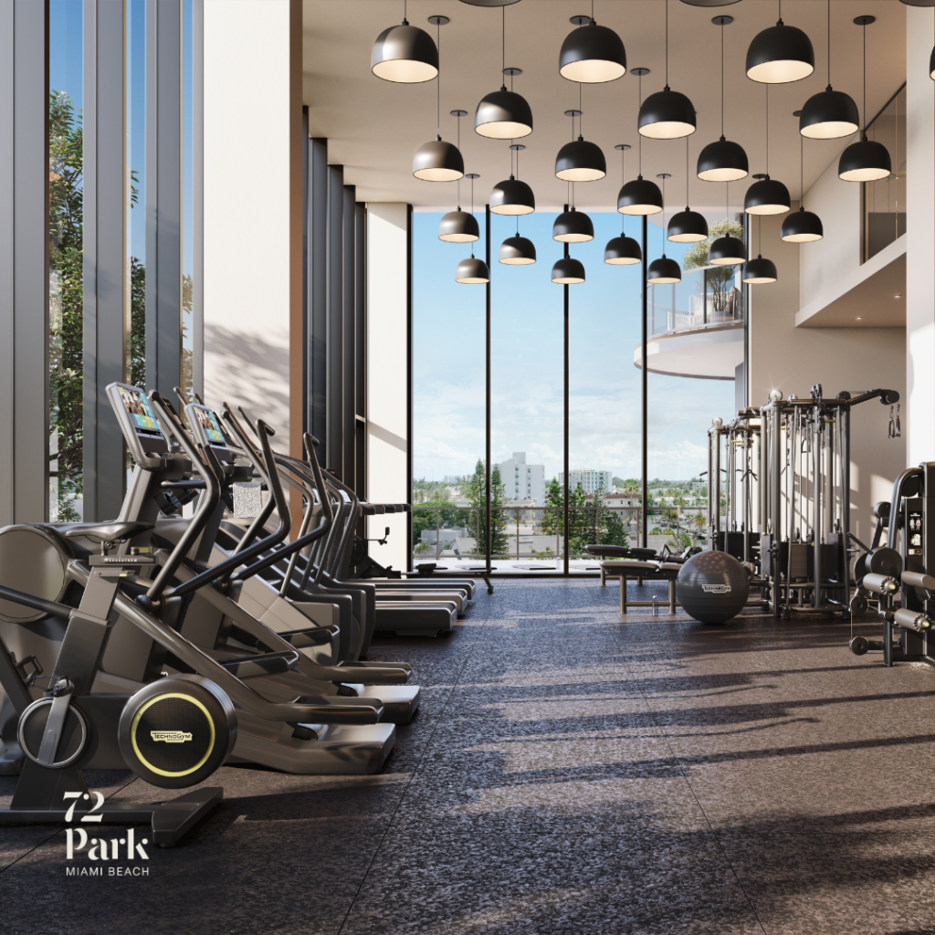 A modern, high-ceilinged luxury gym at 72 Park featuring a row of professional Technogym treadmills and ellipticals. The room is illuminated by dozens of sleek, black dome pendant lights hanging from a soaring ceiling. Massive floor-to-ceiling windows offer a bright view of the Miami Beach skyline and tropical greenery outside.